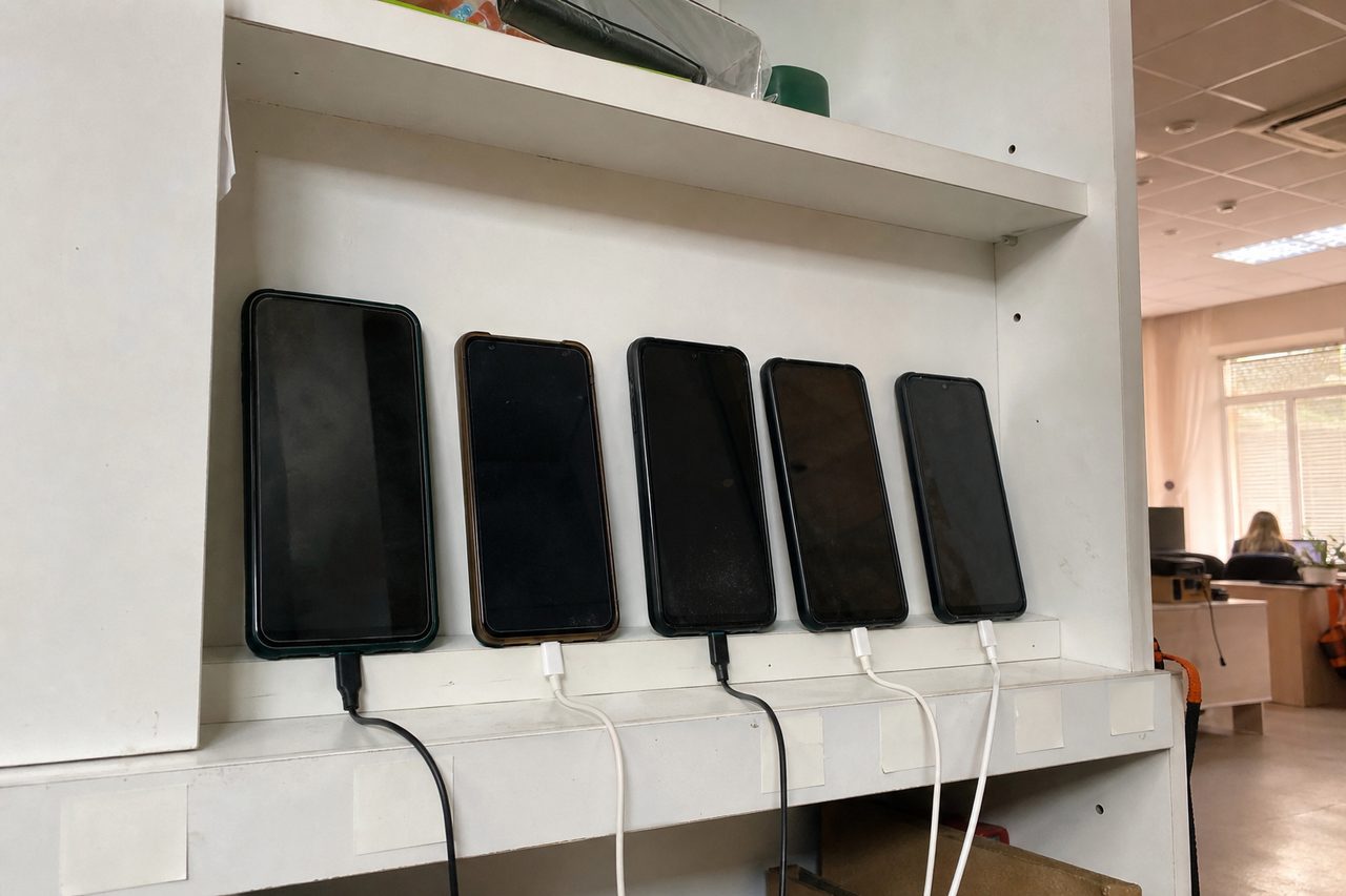 Несколько старых смартфонов на зарядке стоят в ряд на офисной полке