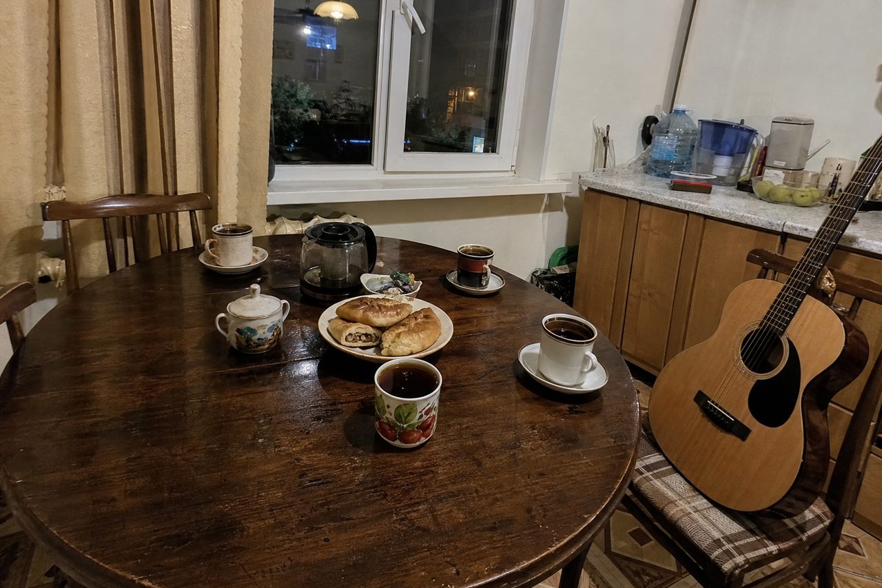 Кухонный стол с чашками и пирогами, к стулу прислонена акустическая гитара