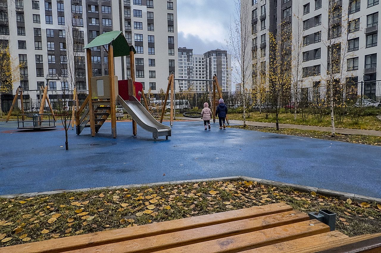Детская площадка во дворе новостройки и желтеющие берёзы пасмурным днём