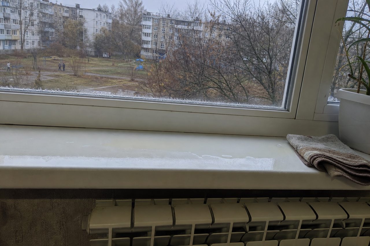 Капли конденсата по нижнему краю пластикового окна и лужица на широком подоконнике над батареей