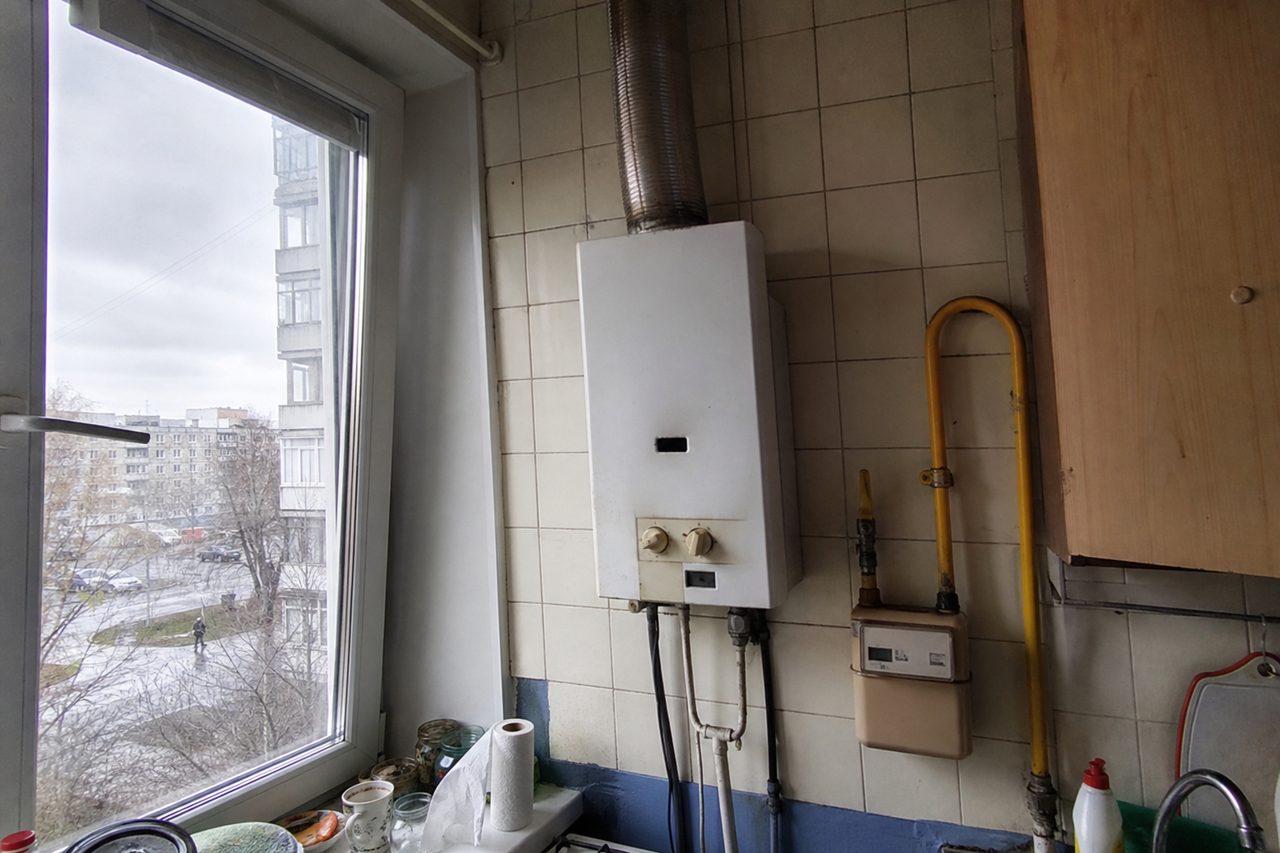 Газовая колонка на кафельной стене кухни и газовый счётчик под ней