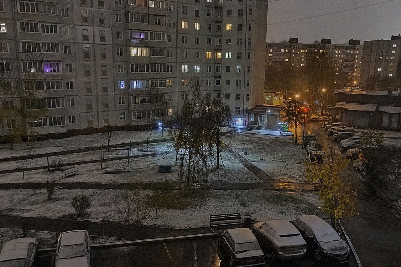 Двор панельных домов вечером, тонкий слой первого снега на траве и крышах машин